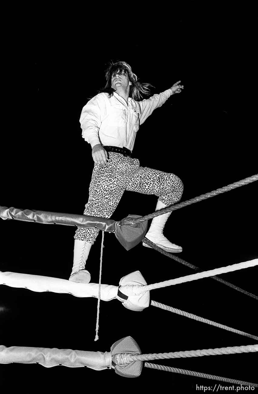 Babyface wrestler works the crowd on the top rope at professional wrestling match.