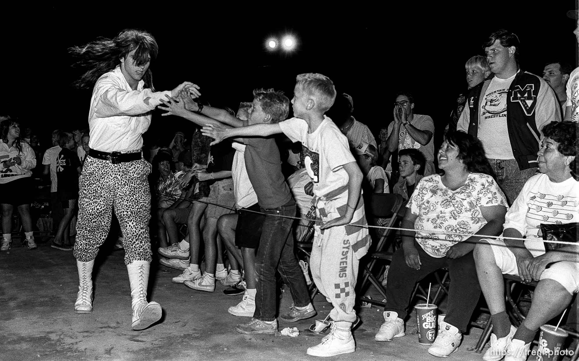 Babyface wrestler high-fives crowd as he makes his entrance at professional wrestling match.