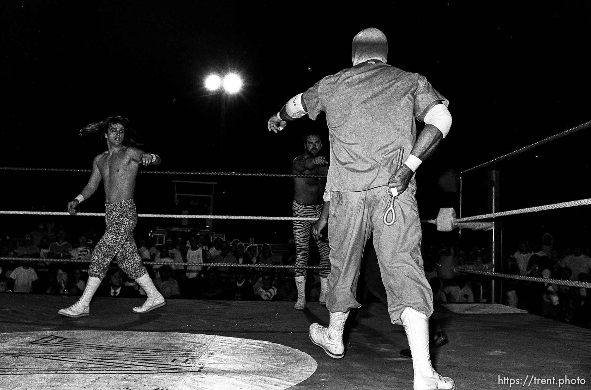 Heel wrestler approaches concerned babyface wrestler with illegal object behind his back at professional wrestling match.