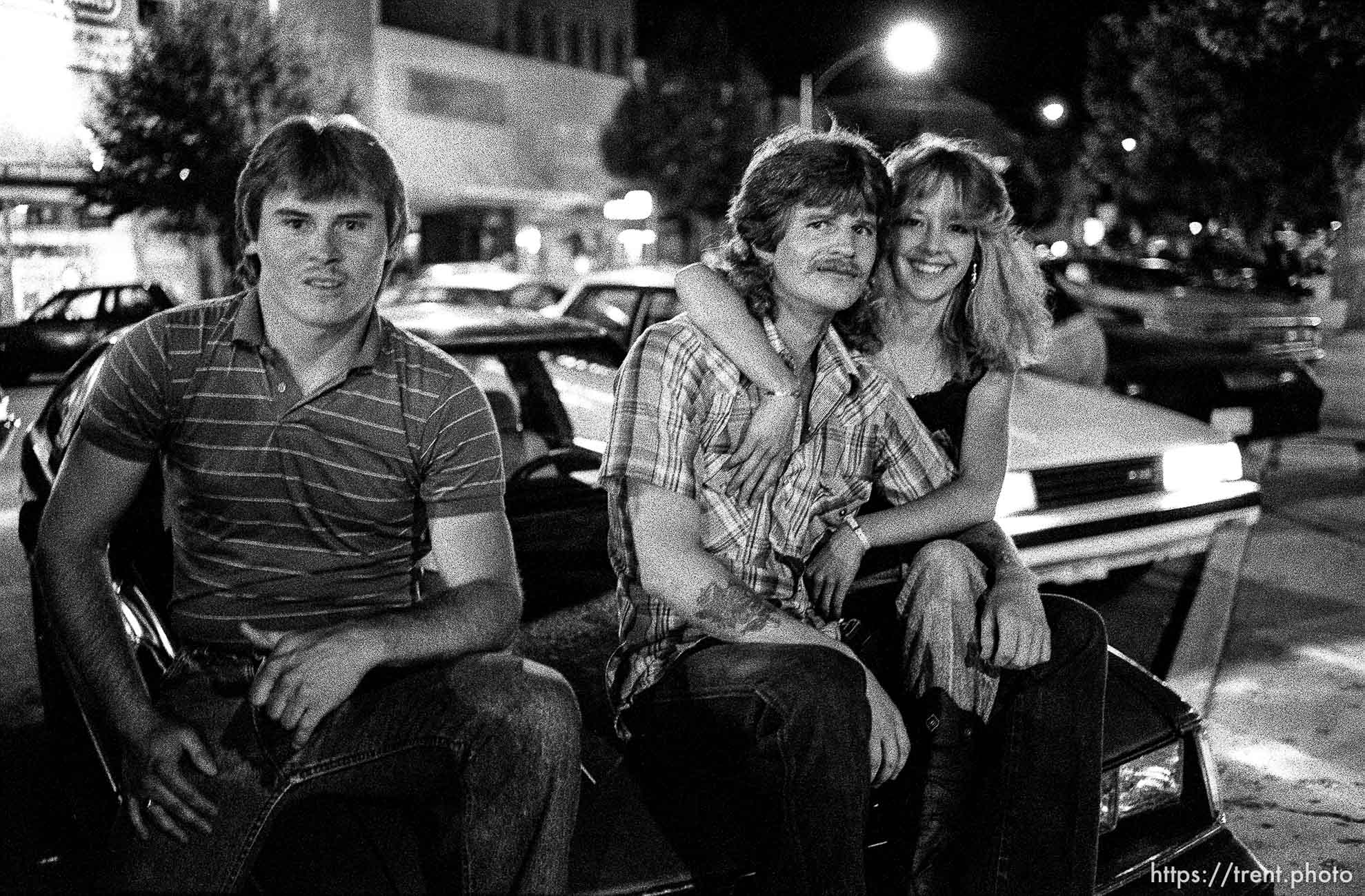 People sitting on their car on Center Street at night.