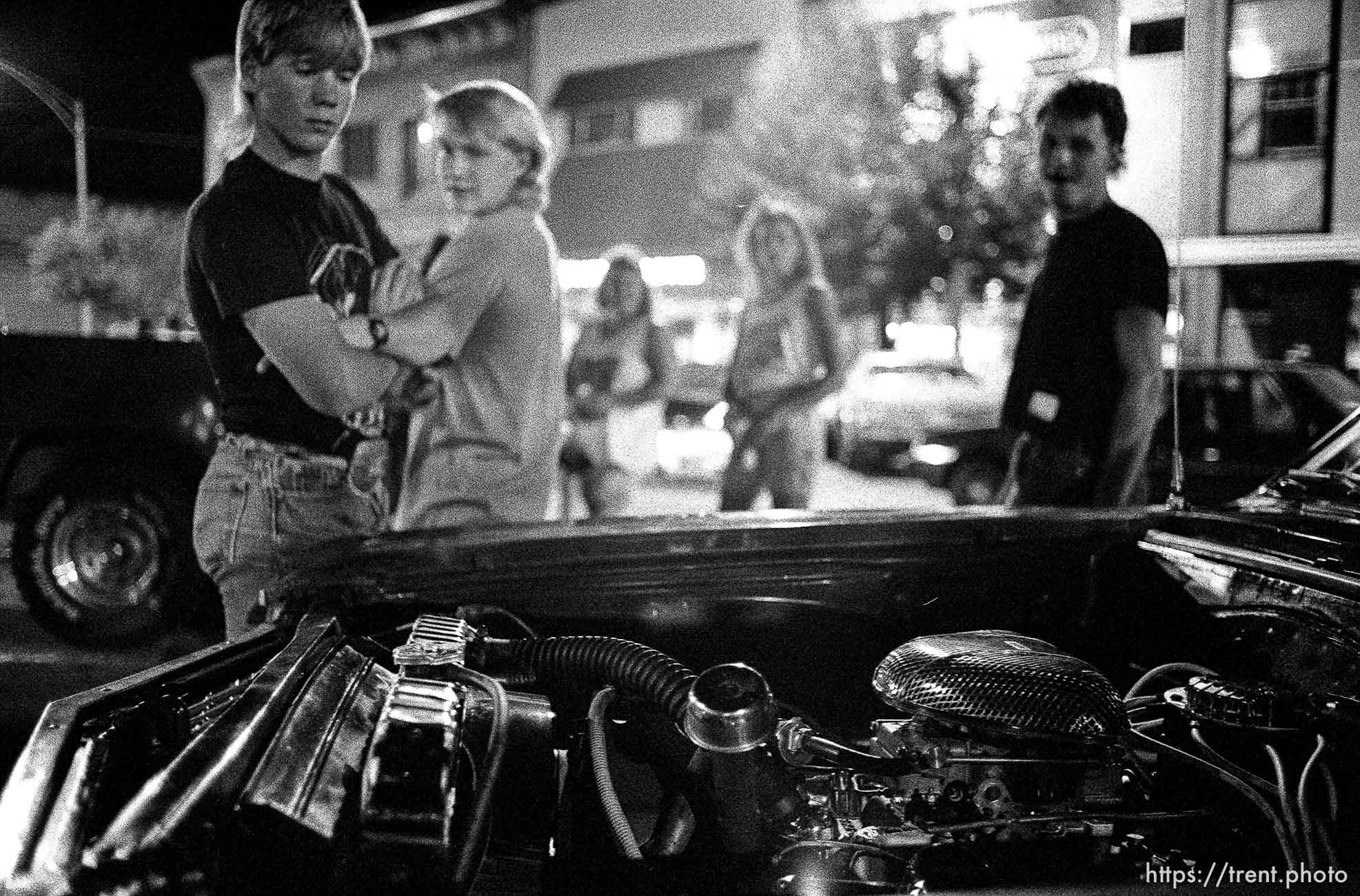 Kids checking out car's engine on Center Street at night.