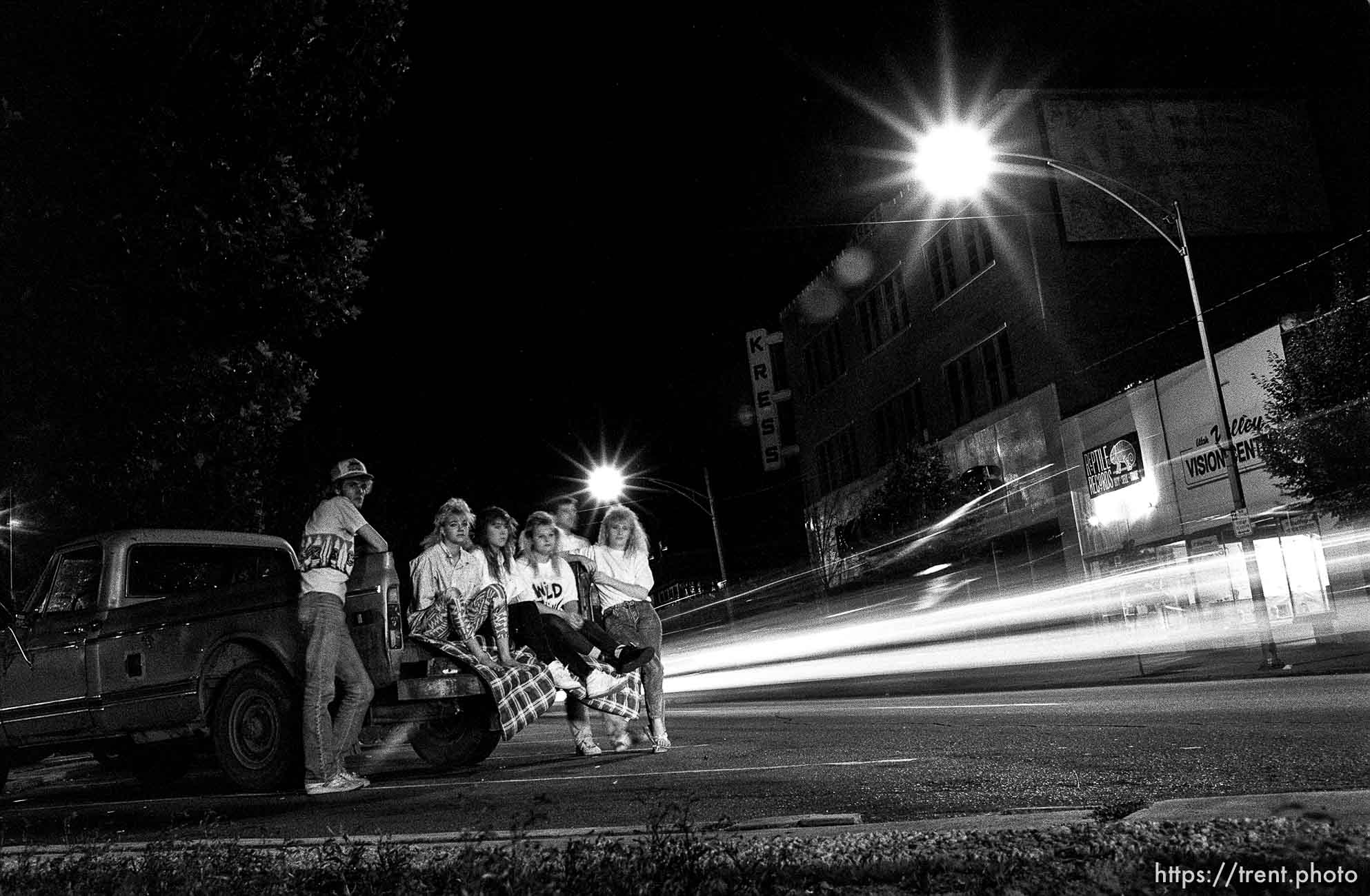 People sit on a truck while others cruise center on Center Street at night.