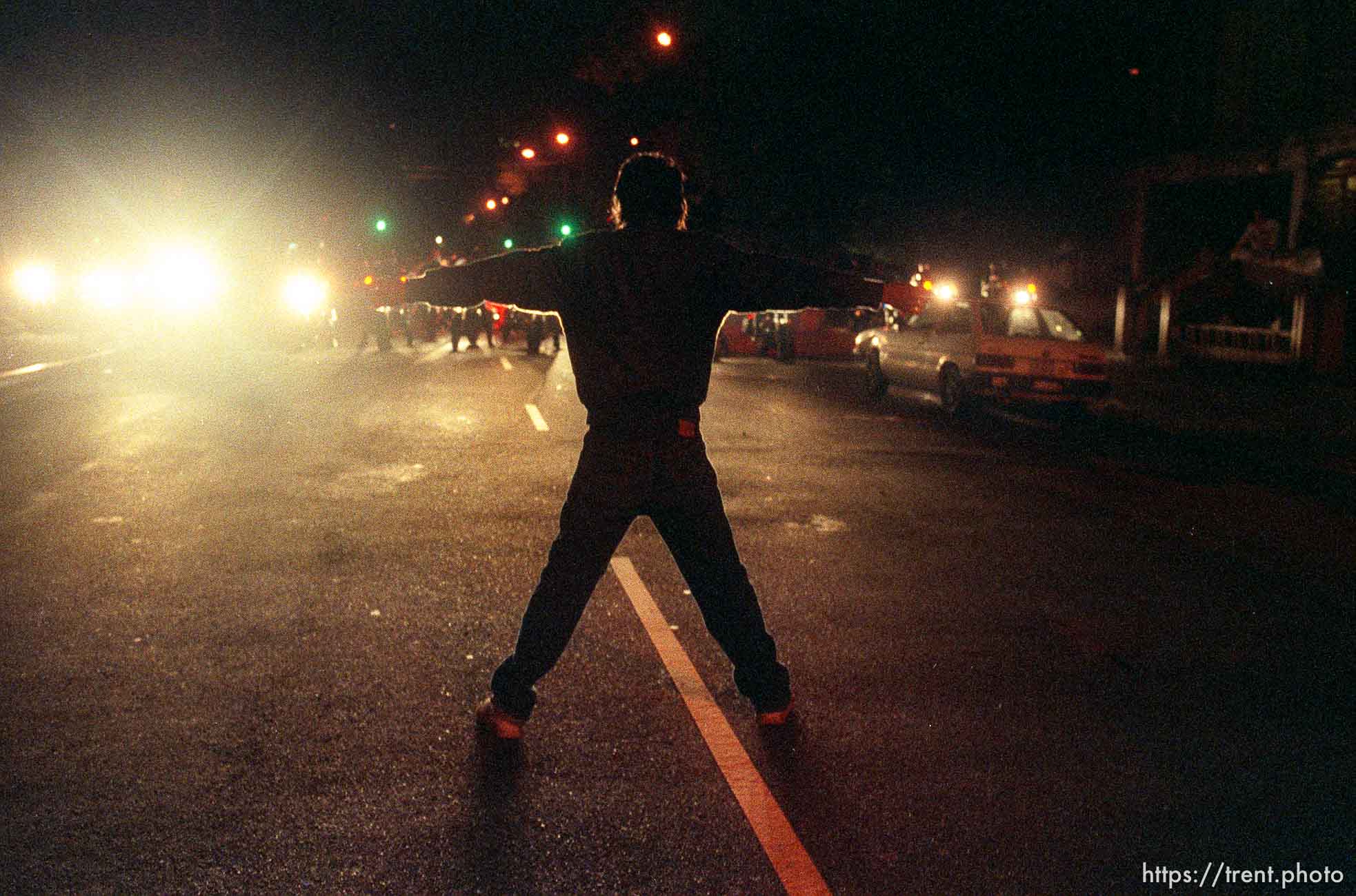 Man stands in middle of street opposing police officers on motorcycles during riots and protests.