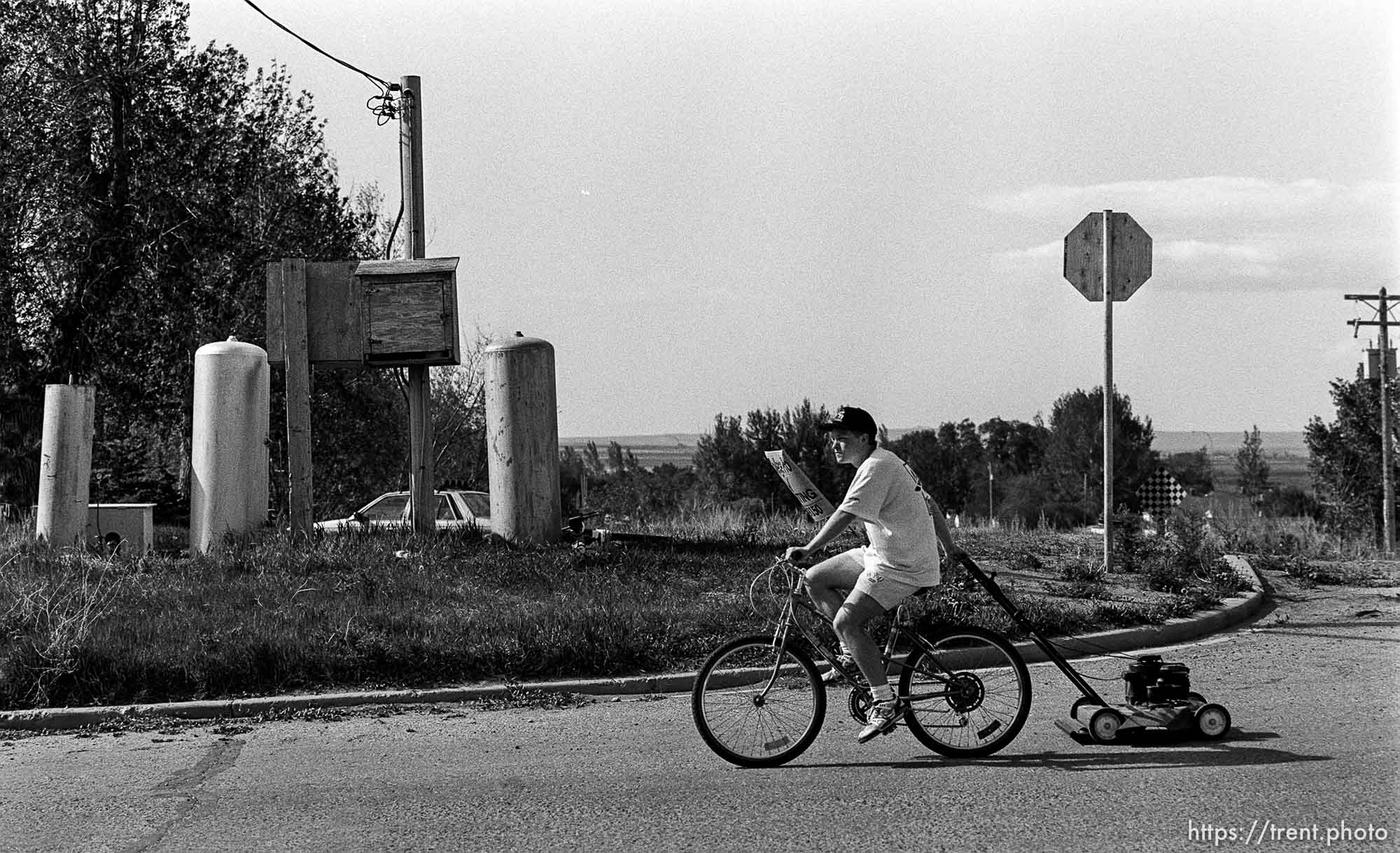 Kid riding bike, pulling lawn mower