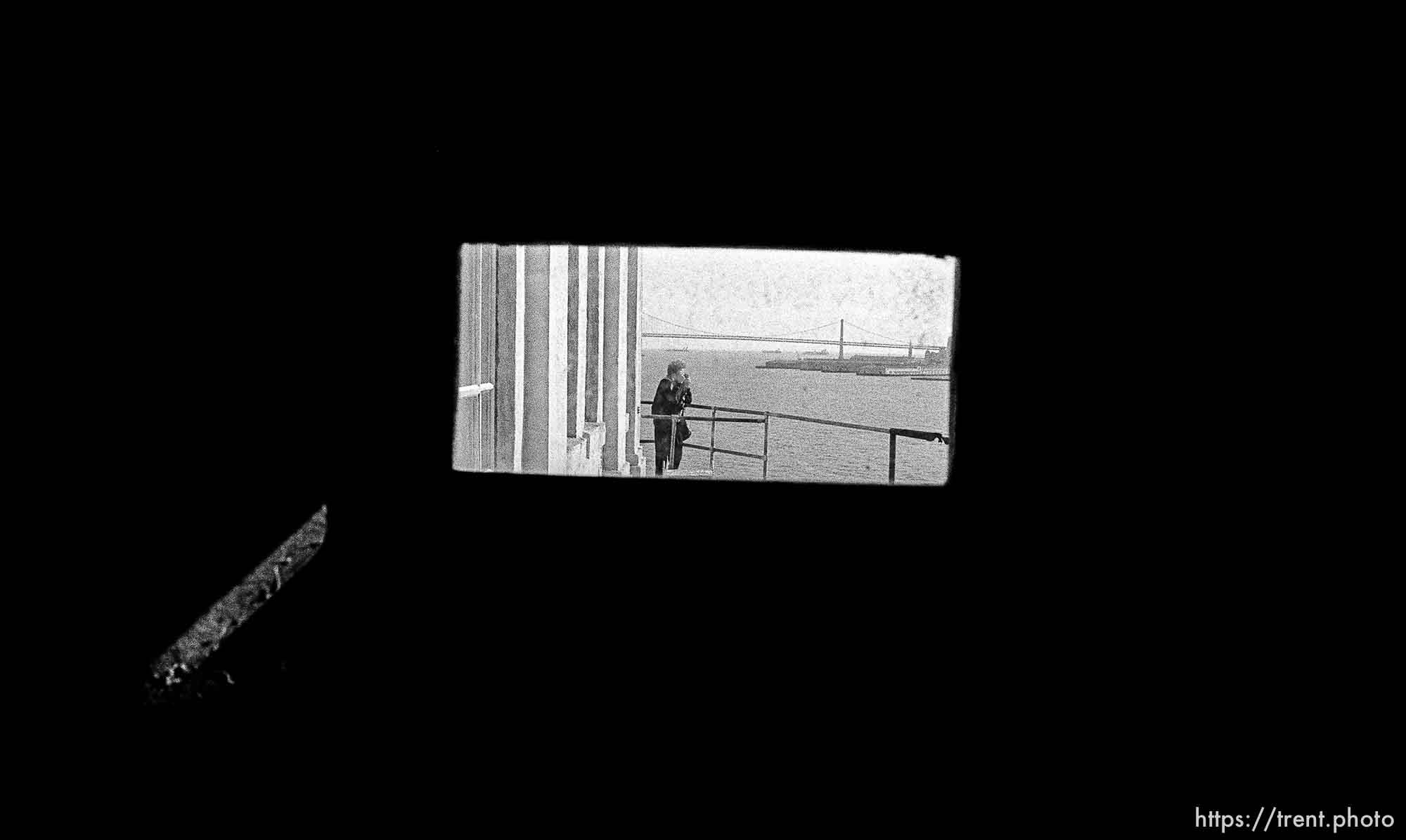 Woman takes a photo and Bay Bridge through tiny window at Alcatraz