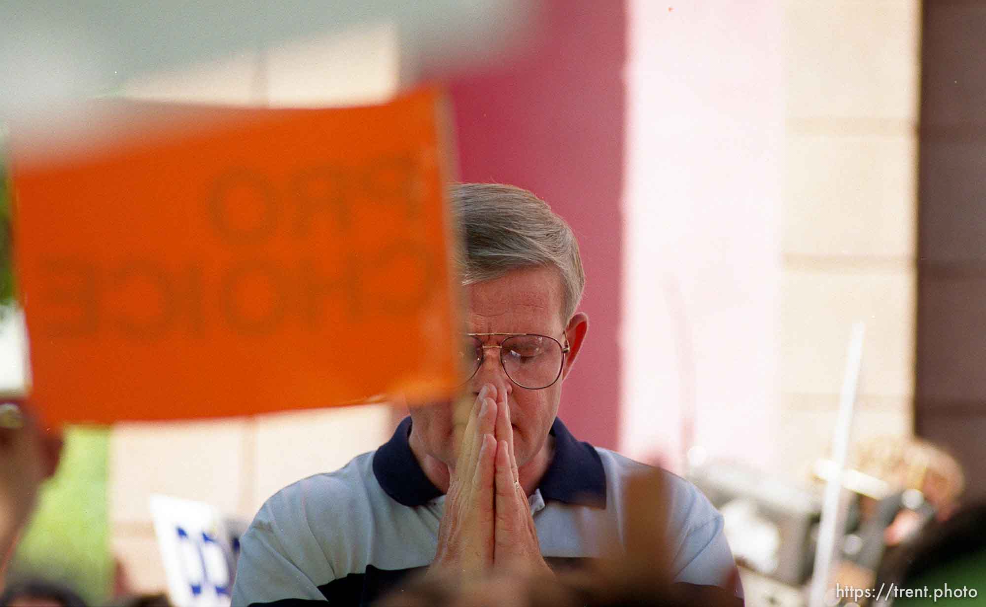 Pro-life man prays amid pro-choice signs at Operation Rescue abortion protest at Planned Parenthood clinic.