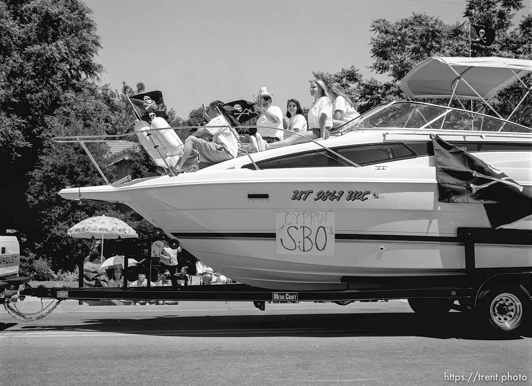 People on boat, waving, at the 4th of July parade on Main Street.