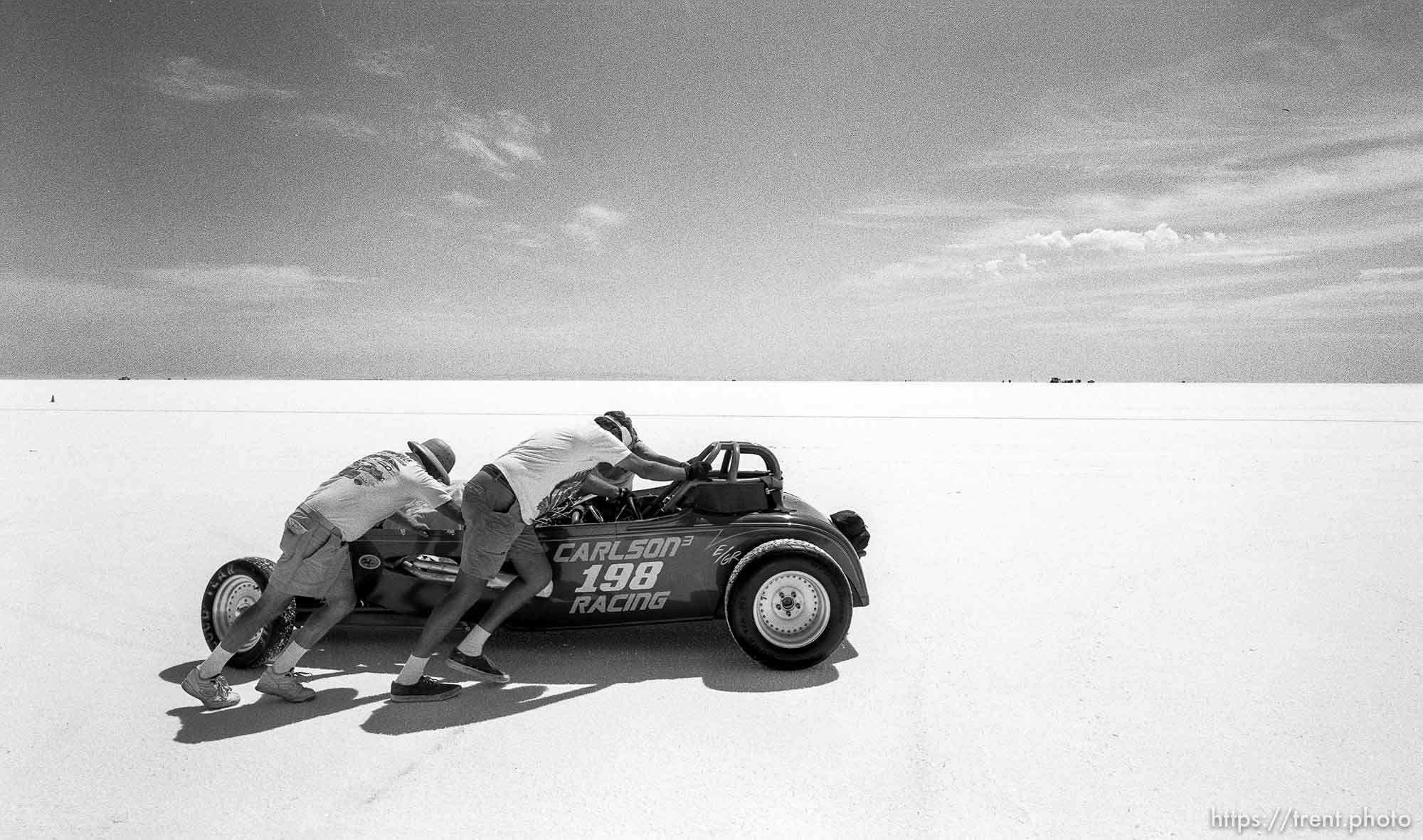 Men push a car at the Bonneville Salt Flats to watch Speed Week.