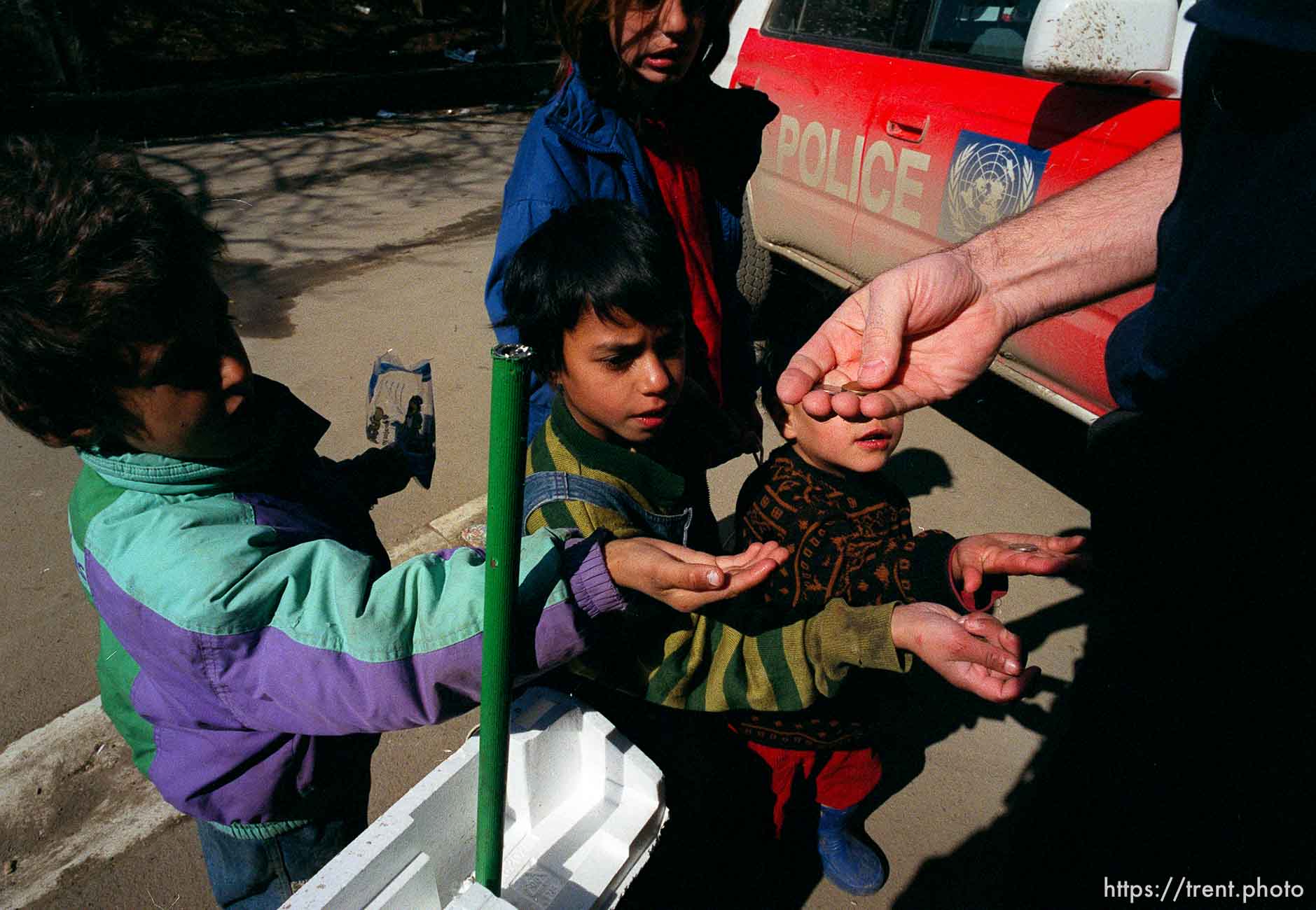 UNMIK police officer Zane Smith hands coins to Roma  children outside the UNMIK police station.