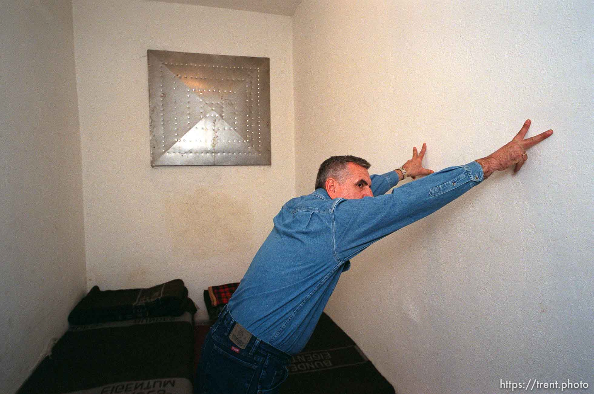 Redzo Kurbegovic demonstrates how he was forced to lean against the wall, his hands in a three-fingered Serbian salute, while he was beaten by police during a three month imprisonment in this police station cell.