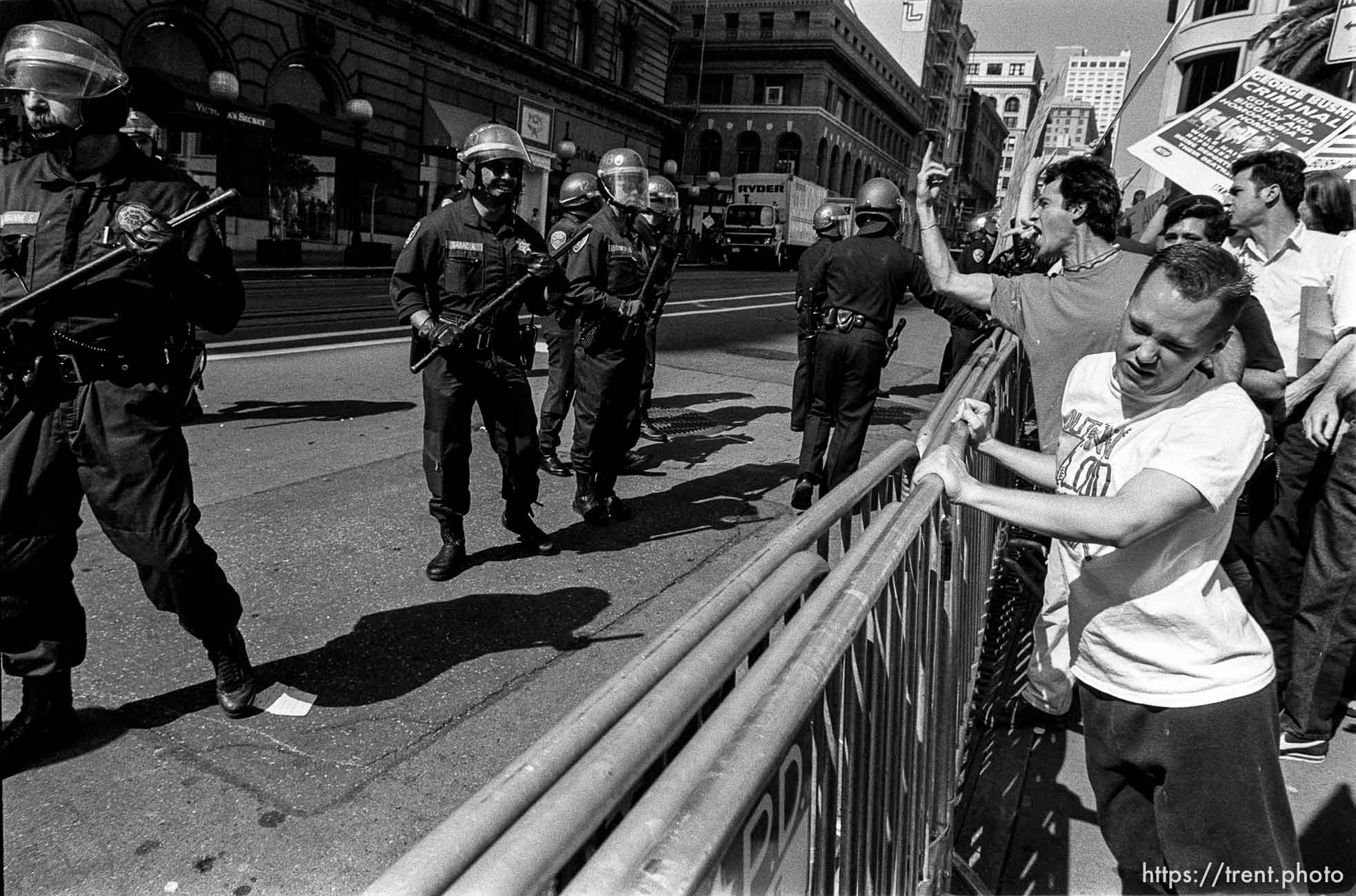 Guy flips off police whil people pull at barricades at Act-Up protest during visit of President Bush