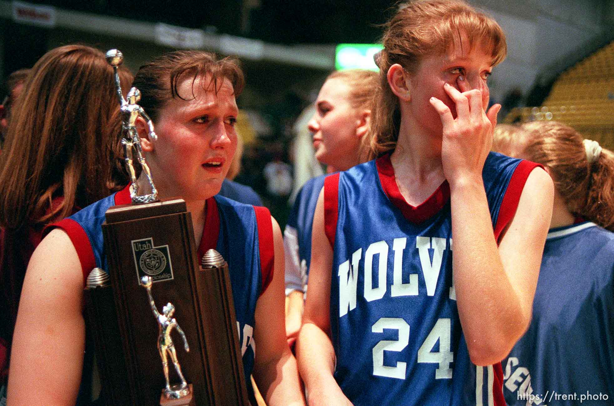 North Sevier basketball players Ann Braithwaite and Shadoe Shaheen (left) hold the second place trophy and grieve while the state champion Beaver Beavers celebrate their victory.