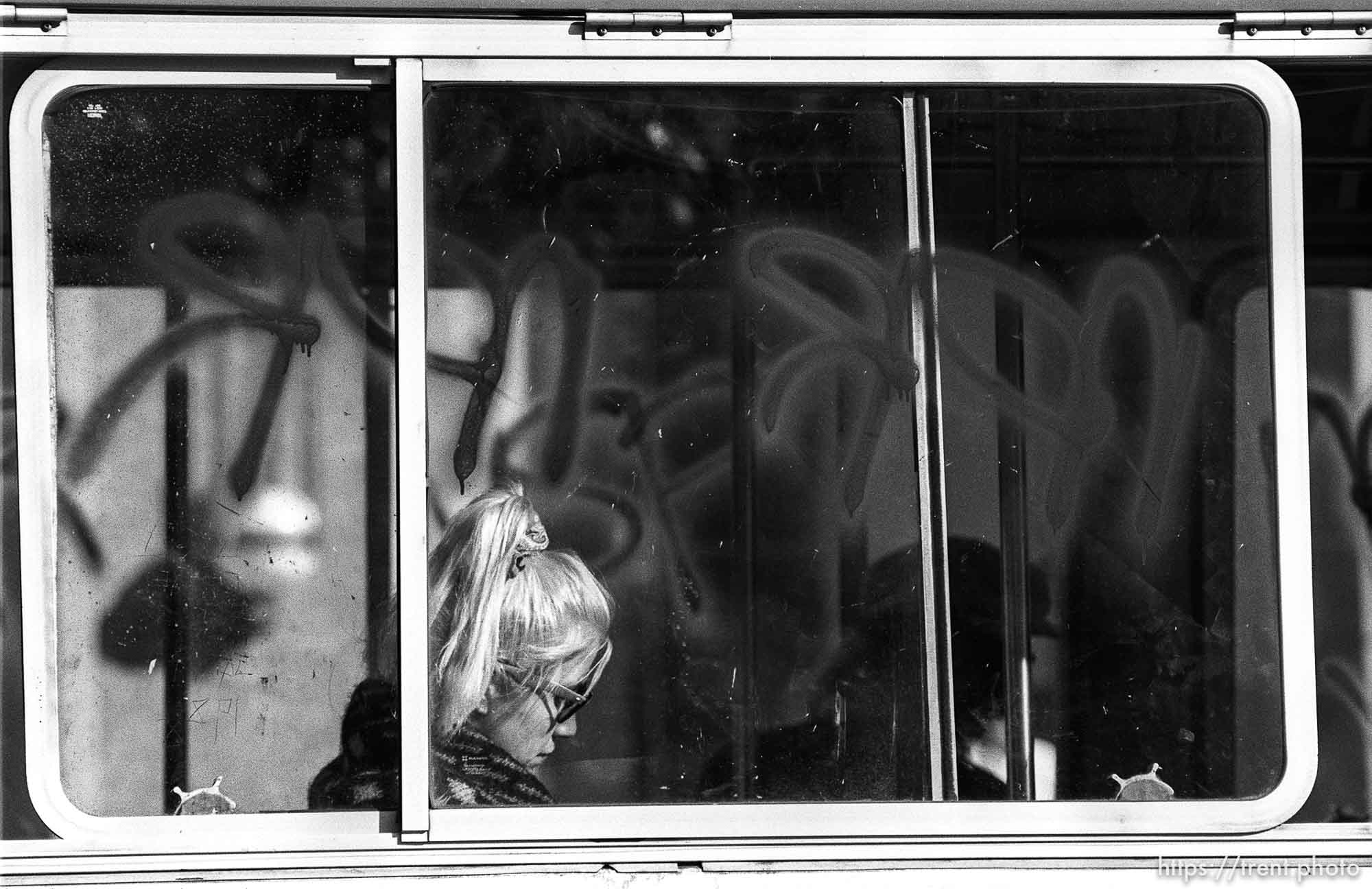 Woman on bus with graffiti on window.