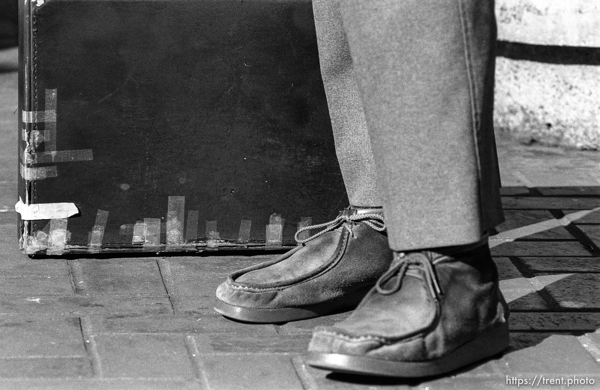 Man's feet and taped up briefcase.