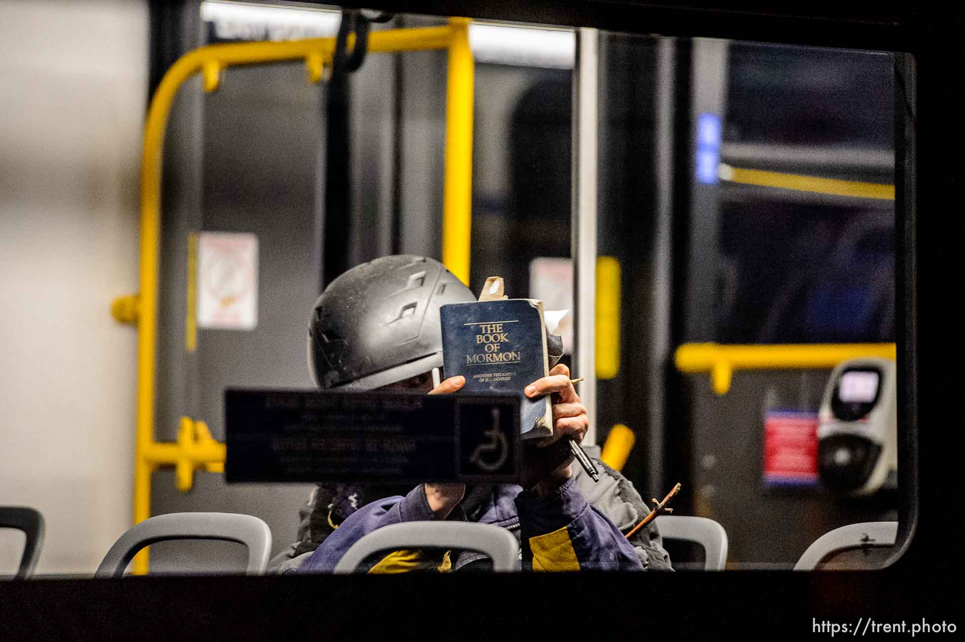 Man wearing a helmet on a bus hiding behind the Book of Mormon