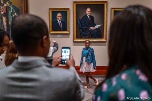 (Trent Nelson  |  The Salt Lake Tribune) A young girl poses under a portrait of Russell M. Nelson at General Conference on Sunday, Oct. 6, 2024. At left is a portrait of Dallin H. Oaks.